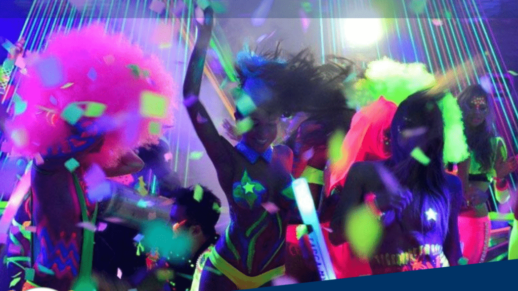 Group of individuals in neon costumes dancing under colorful lights at a party.