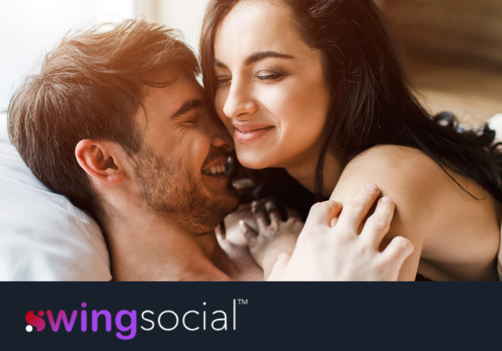 A smiling man and woman in bed together. Header image for a post about swinger lifestyle definition, terms, and 101 guide to swinging. Also includes SwingSocial logo.